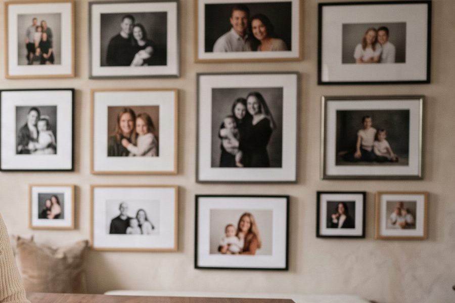 A wall densely hung with framed family portraits in warm light