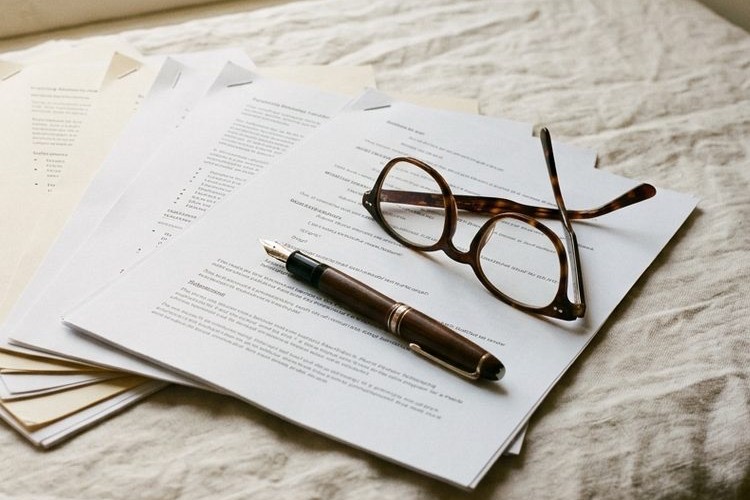 A printed studio script page lying on linen with a fountain pen and reading glasses resting across it