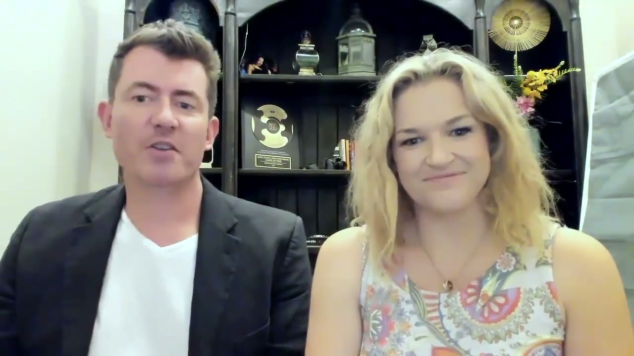 Mike and Jonelle Beveridge teaching on camera in a course lesson, seated side by side in front of a dark timber shelf